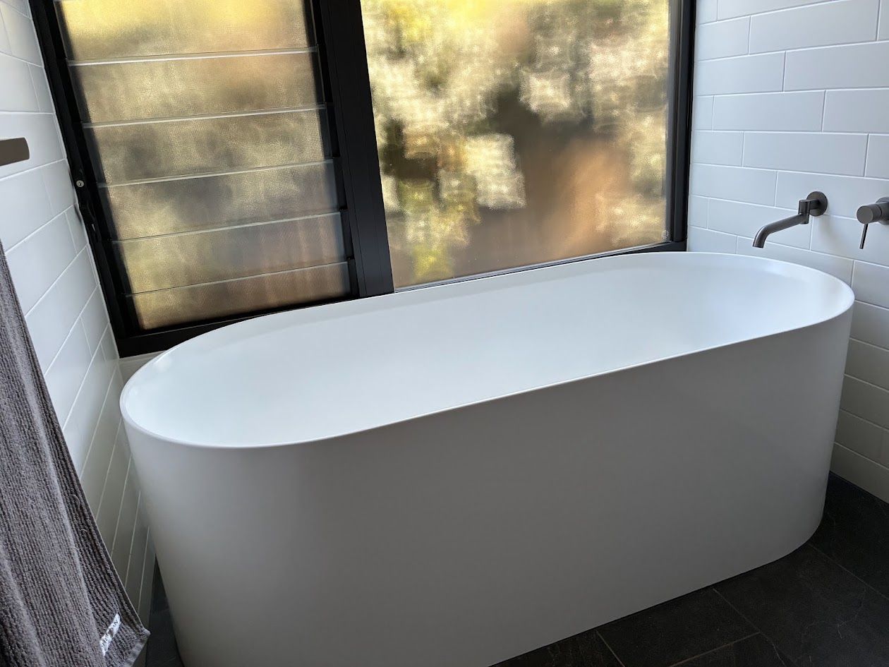 Freestanding white bath beneath frosted louvre windows with subway tiles