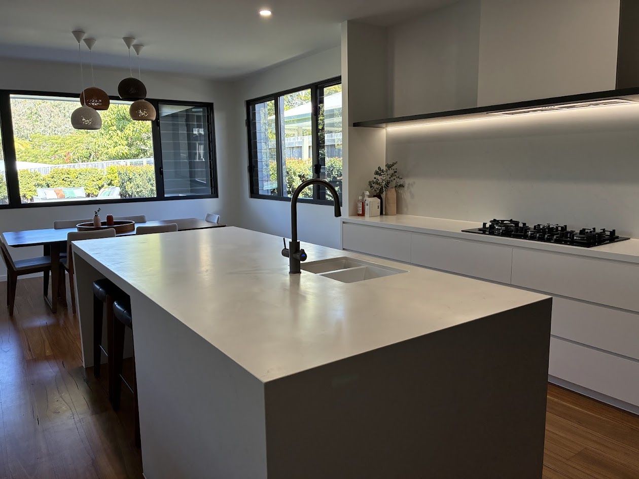White stone kitchen island and cooktop bench with dining area and garden windows behind
