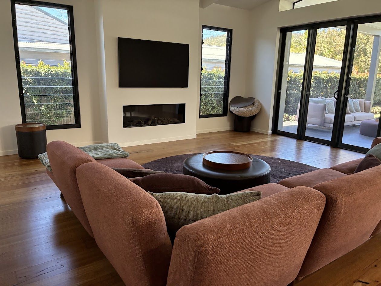 Light-filled living room with timber floors, louvre windows and sliding doors to a covered deck