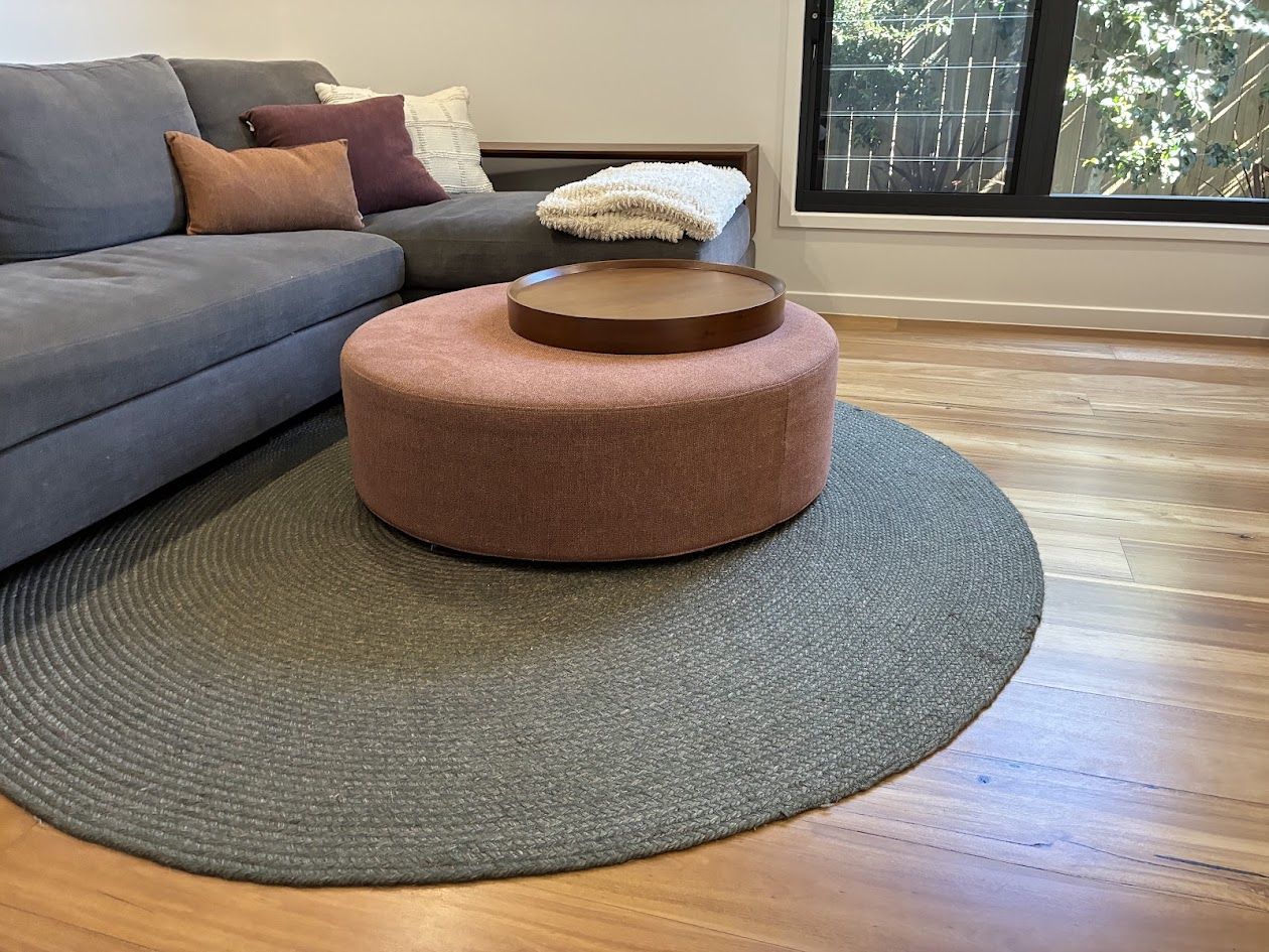 Grey sofa, round pink ottoman and braided rug on timber floors